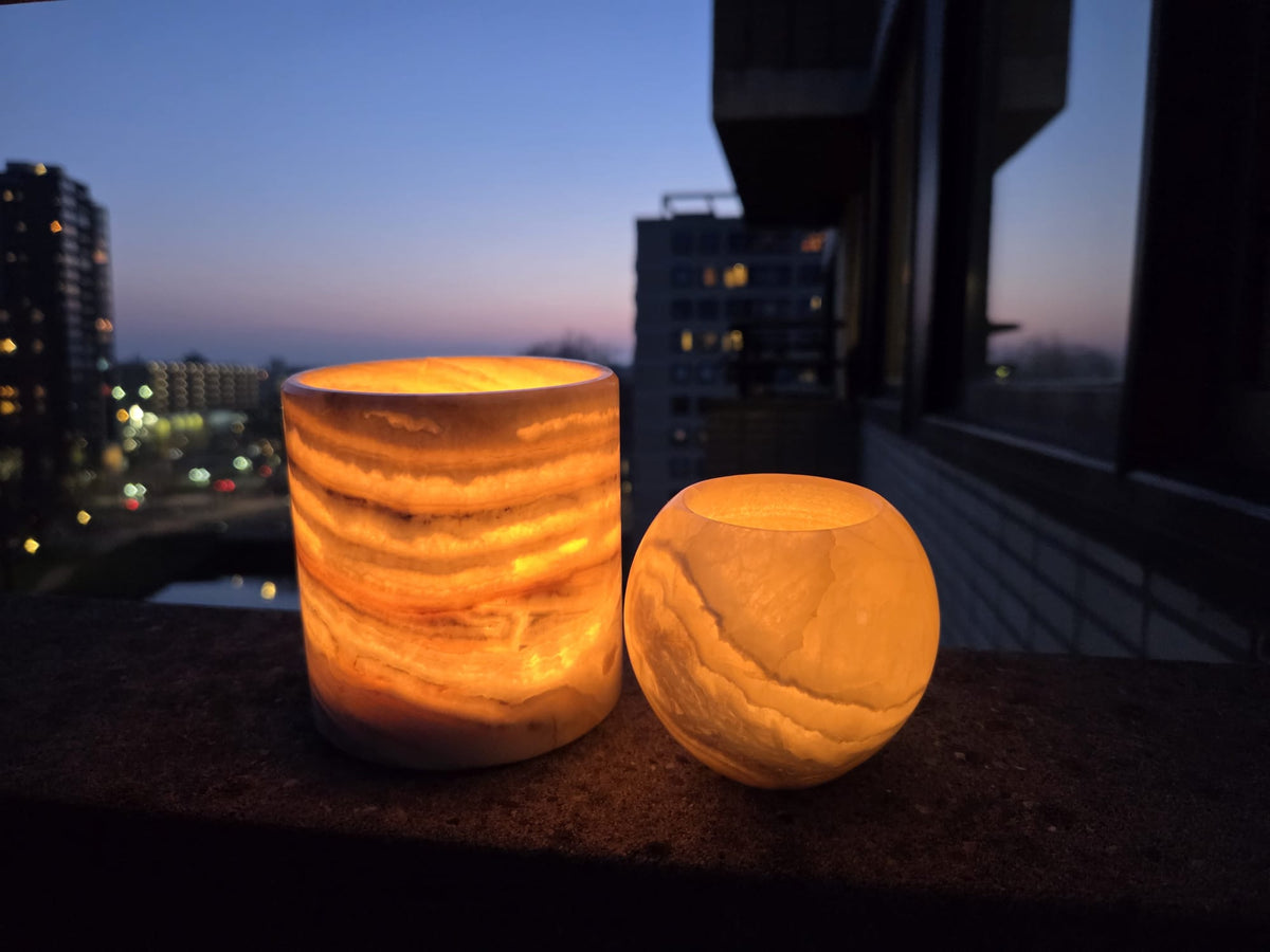 Two Egyptian alabaster candle holders glowing warm amber at dusk against a city skyline