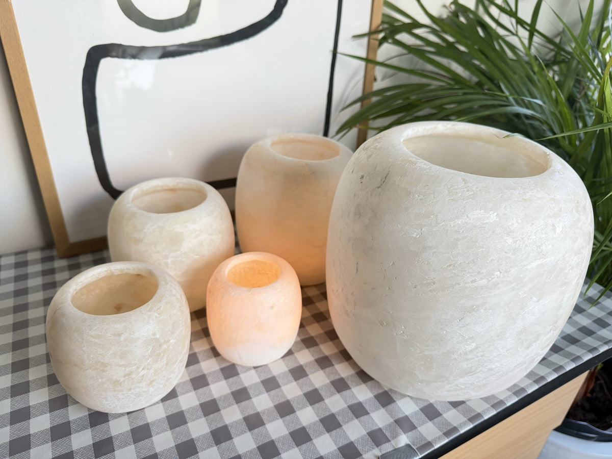 The Pot, five frosted matte alabaster pots from small to extra large on a checked cloth, two of them lit and glowing warm orange