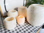 The Pot, the five frosted pots from a closer angle, open rims and clouded matte stone, two of them lit and glowing orange inside
