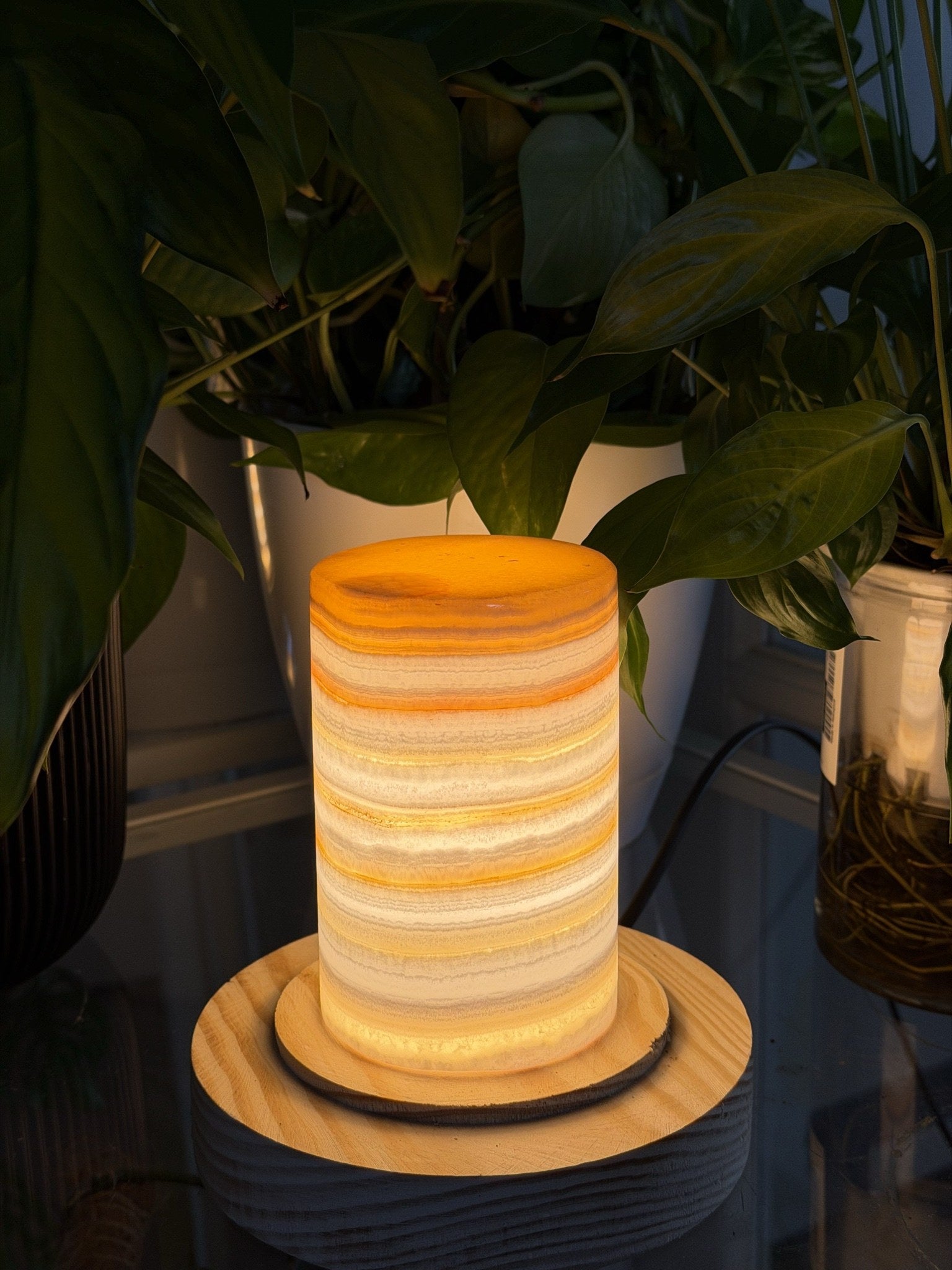 Polished alabaster tealight vessel glowing against a checked fabric backdrop with plant leaves overhead