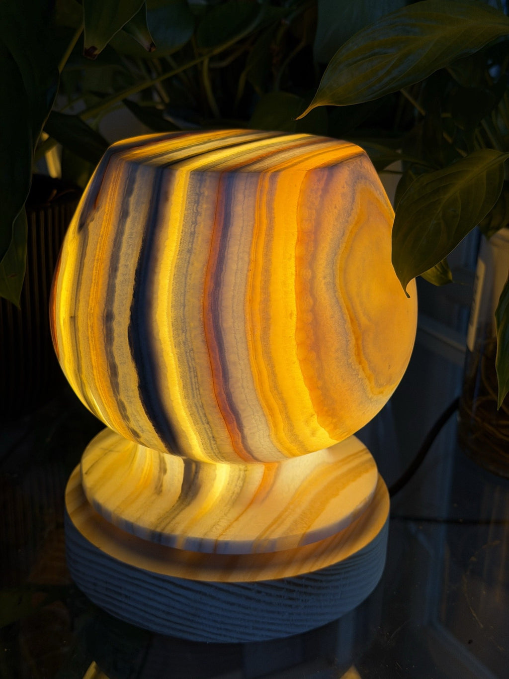 The Barrel alabaster lamp glowing amber, its rounded symmetric form banded in orange and grey on a ridged wood base