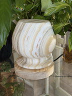 The Barrel alabaster lamp unlit, cream stone with soft tan banding on a flat alabaster collar and grooved wood base