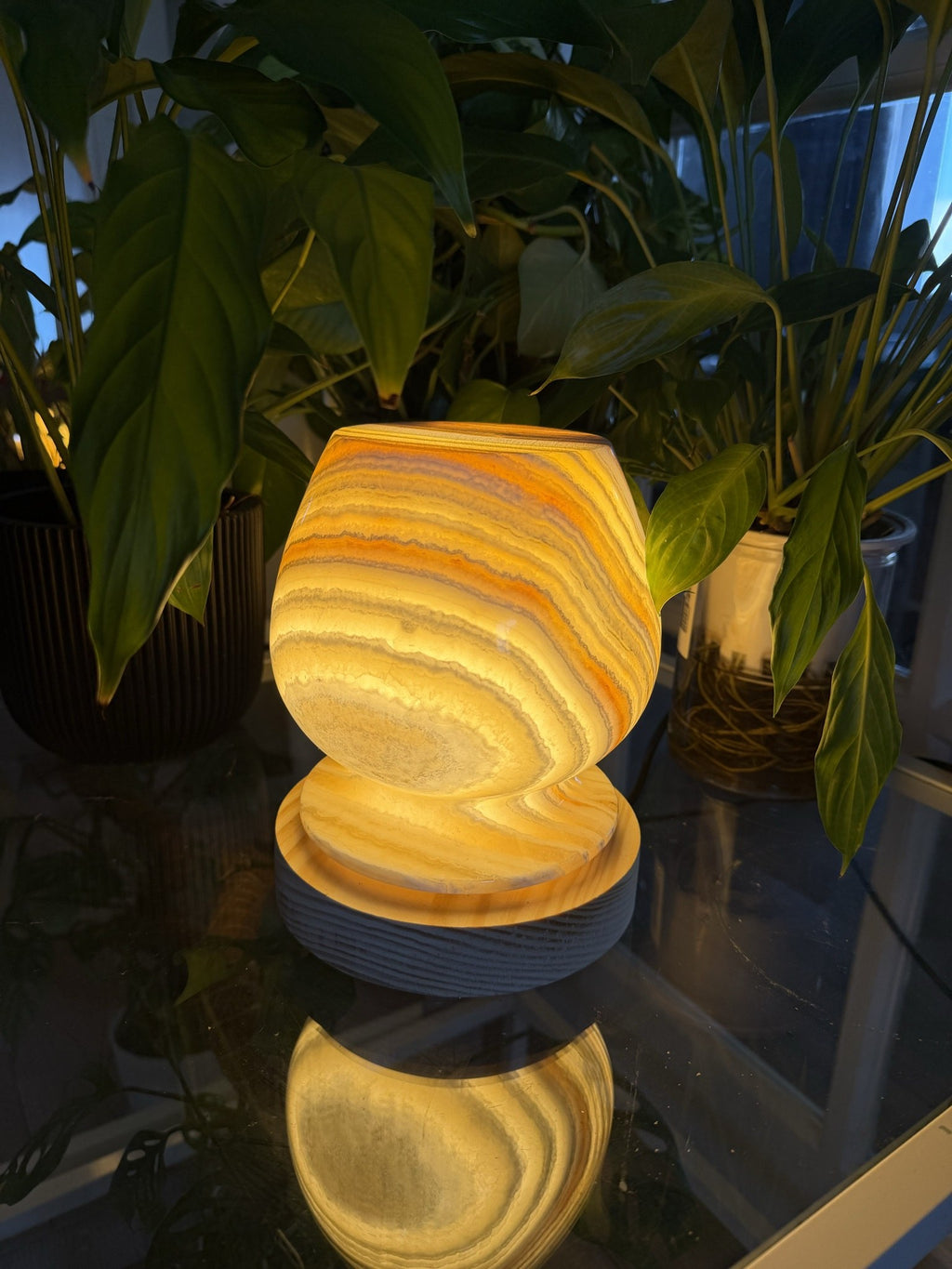 The Boulder lit, a rounded turned alabaster lamp glowing amber with concentric ring banding, on an alabaster collar and ridged wood base