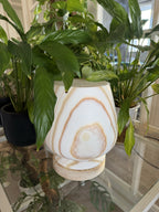 The Boulder unlit in daylight, cream alabaster with soft tan concentric rings and a pale oval marking, framed by houseplants