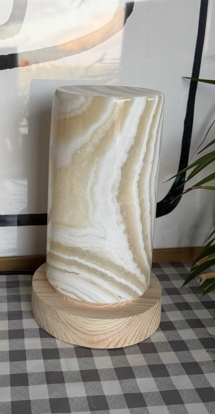 The Pillar L unlit in daylight, a tall alabaster column with olive and cream wavy banding on a turned wood base