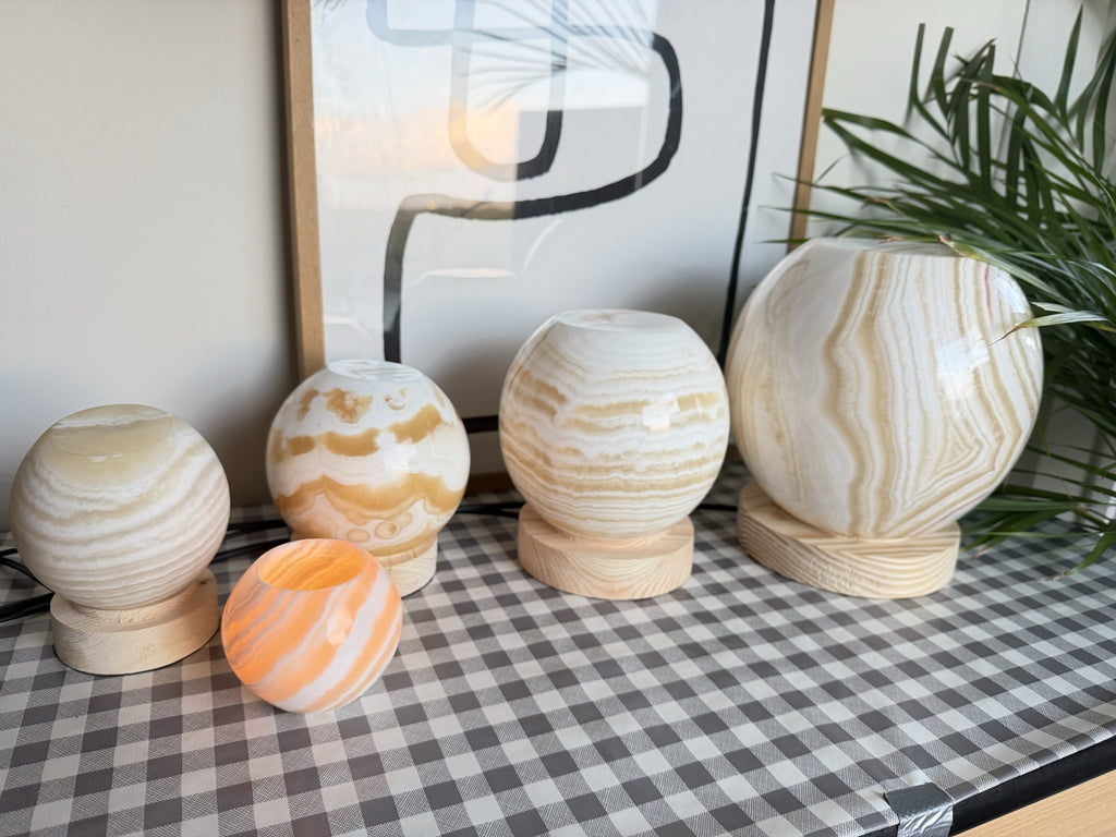 The Sphere, four unlit polished alabaster balls on turned pine bases rising small to extra large, a small orange orb in front for scale