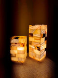 Mosaic Cube Pair lit: two tiled alabaster block lamps, one medium and one taller large, glowing amber on a woven mat in a dark room