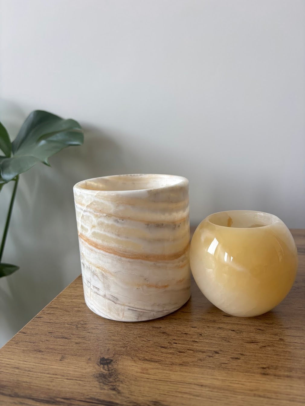 The Duo unlit on a wooden table beside a plant, a pale banded cylinder next to a smaller honey-yellow orb